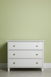 Photo of Modern white chest of drawers near light green wall indoors