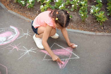 Little child drawing star with chalk on asphalt