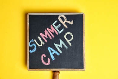 Photo of Words SUMMER CAMP written with colorful chalk on small blackboard, top view