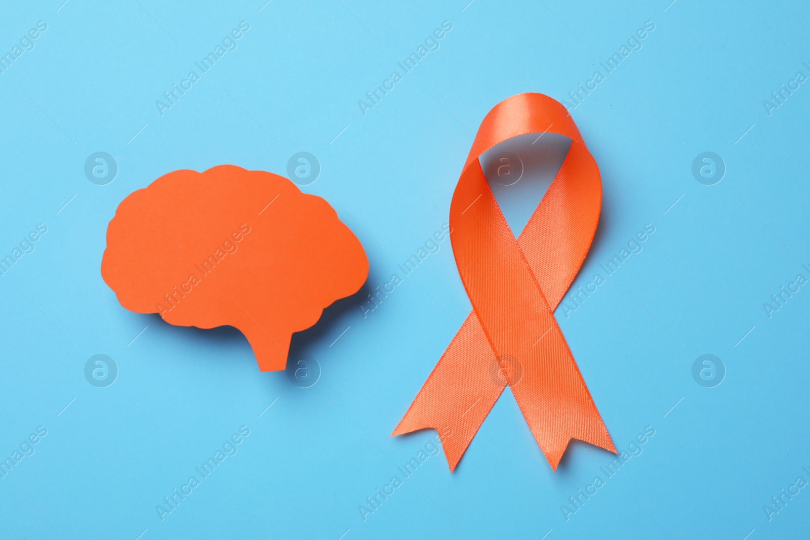Photo of Orange ribbon and paper brain cutout on light blue background, flat lay. Multiple sclerosis awareness