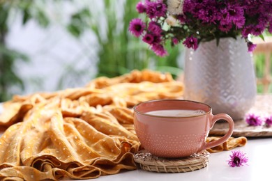 Cup of aromatic coffee, beautiful flowers and orange cloth on white table, space for text