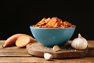 Photo of Composition with bowl of sweet potato chips and garlic on table against black background