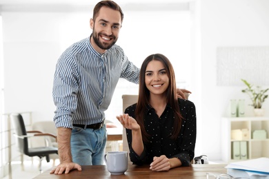 Photo of Happy young couple looking at camera and using video chat in home office