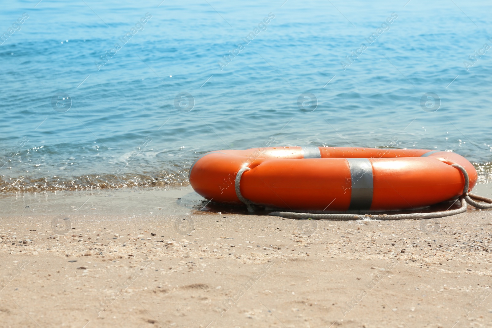 Photo of Orange life buoy on sand near sea. Emergency rescue equipment