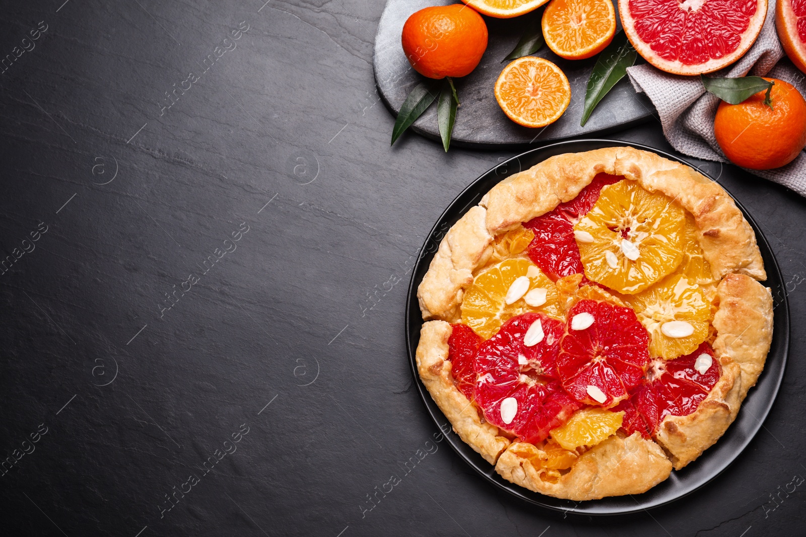 Photo of Tasty galette with citrus fruits on dark grey table, flat lay. Space for text