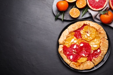 Photo of Tasty galette with citrus fruits on dark grey table, flat lay. Space for text