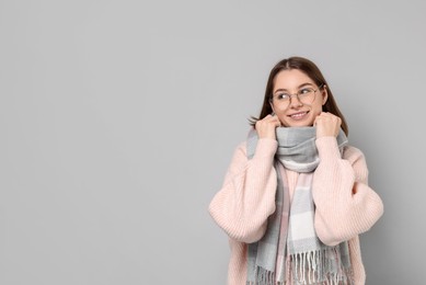 Beautiful woman in warm scarf and glasses on gray background, space for text