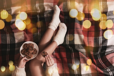 Woman in knitted socks with tasty cookies on warm plaid, top view