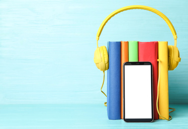 Photo of Books with modern headphones and smartphone on light blue wooden table. Space for text