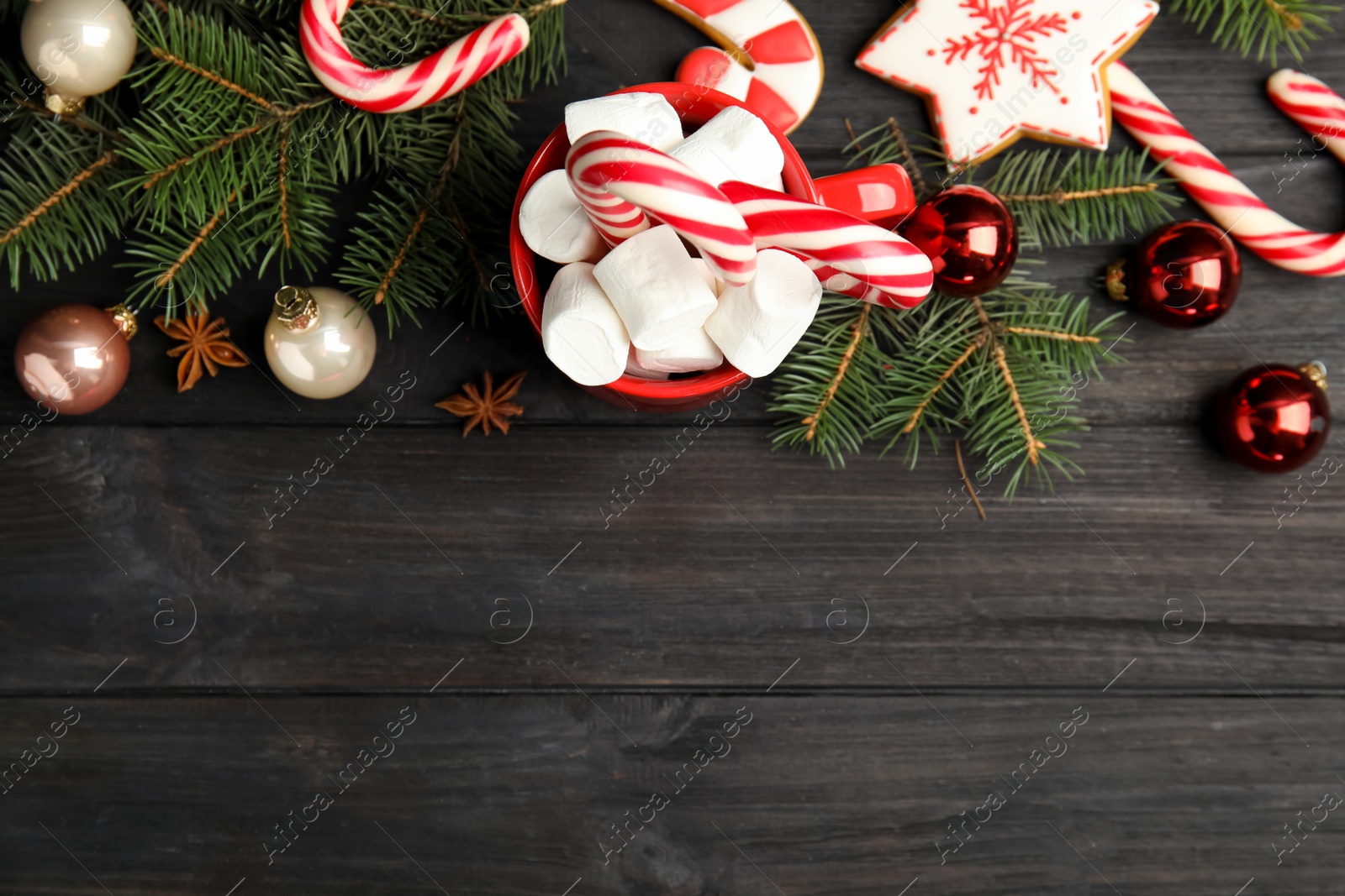 Photo of Cup of tasty cocoa with marshmallows, candy canes and Christmas decor on black wooden table, flat lay. Space for text