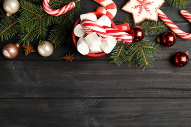 Photo of Cup of tasty cocoa with marshmallows, candy canes and Christmas decor on black wooden table, flat lay. Space for text