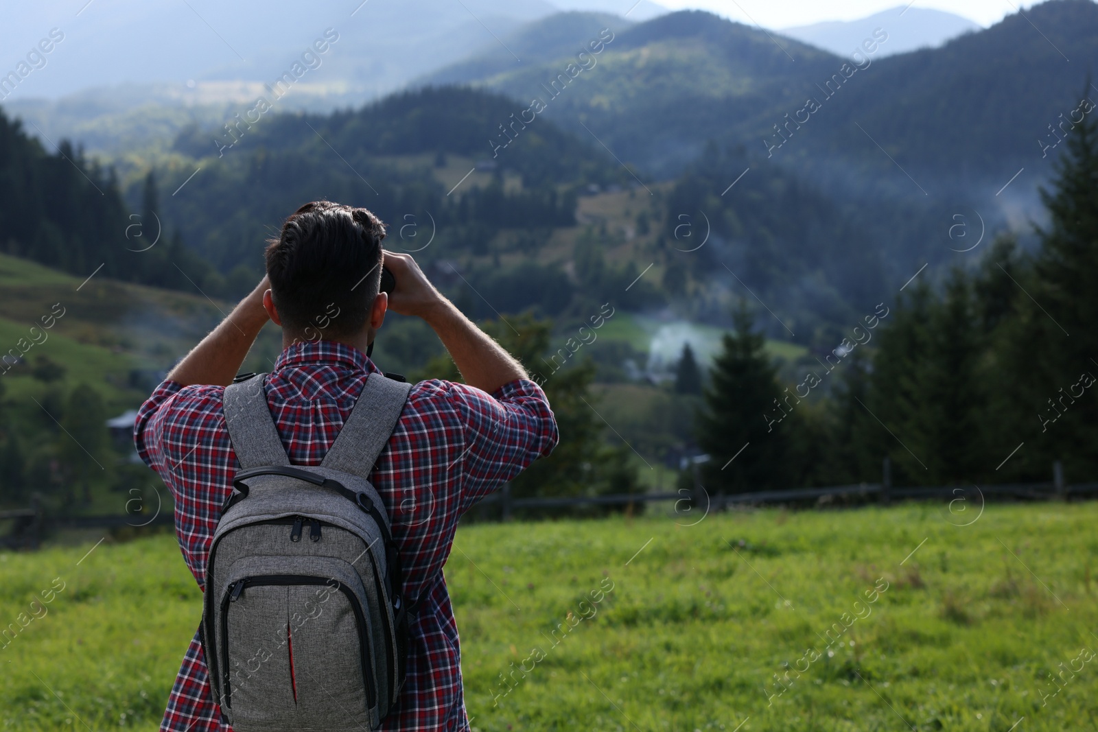 Photo of Tourist with backpack and binoculars enjoying landscape in mountains, back view