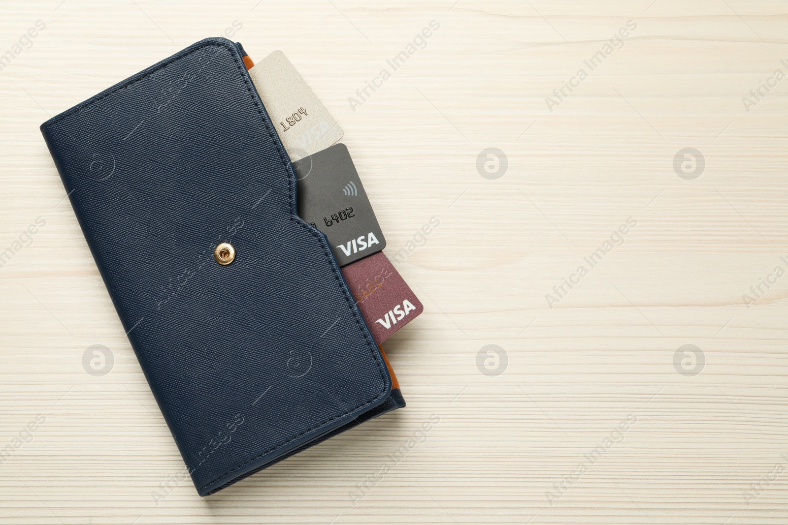 Photo of MYKOLAIV, UKRAINE - FEBRUARY 23, 2022: Bank cards of Visa payment system in leather wallet on wooden table, top view. Space for text