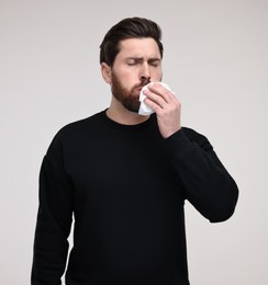 Sick man with tissue coughing on light grey background