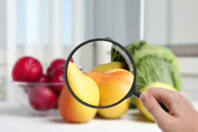Woman with magnifying glass exploring fruits, closeup. Poison detection