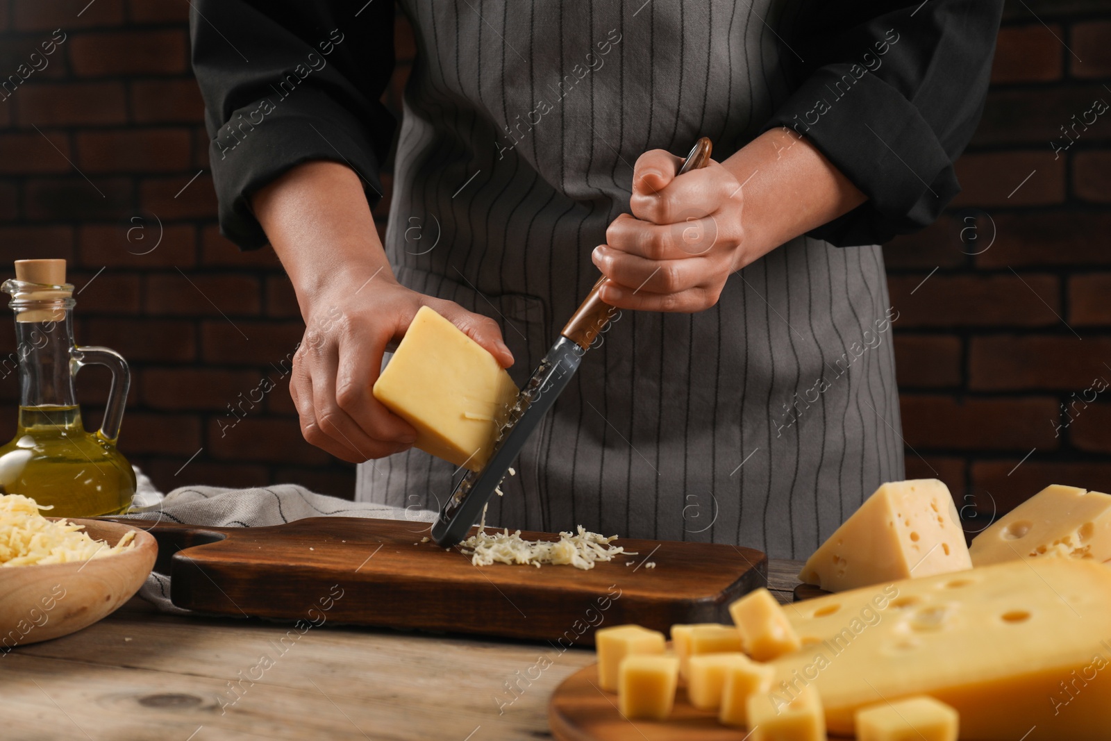 Photo of Woman grating cheese at wooden table, closeup