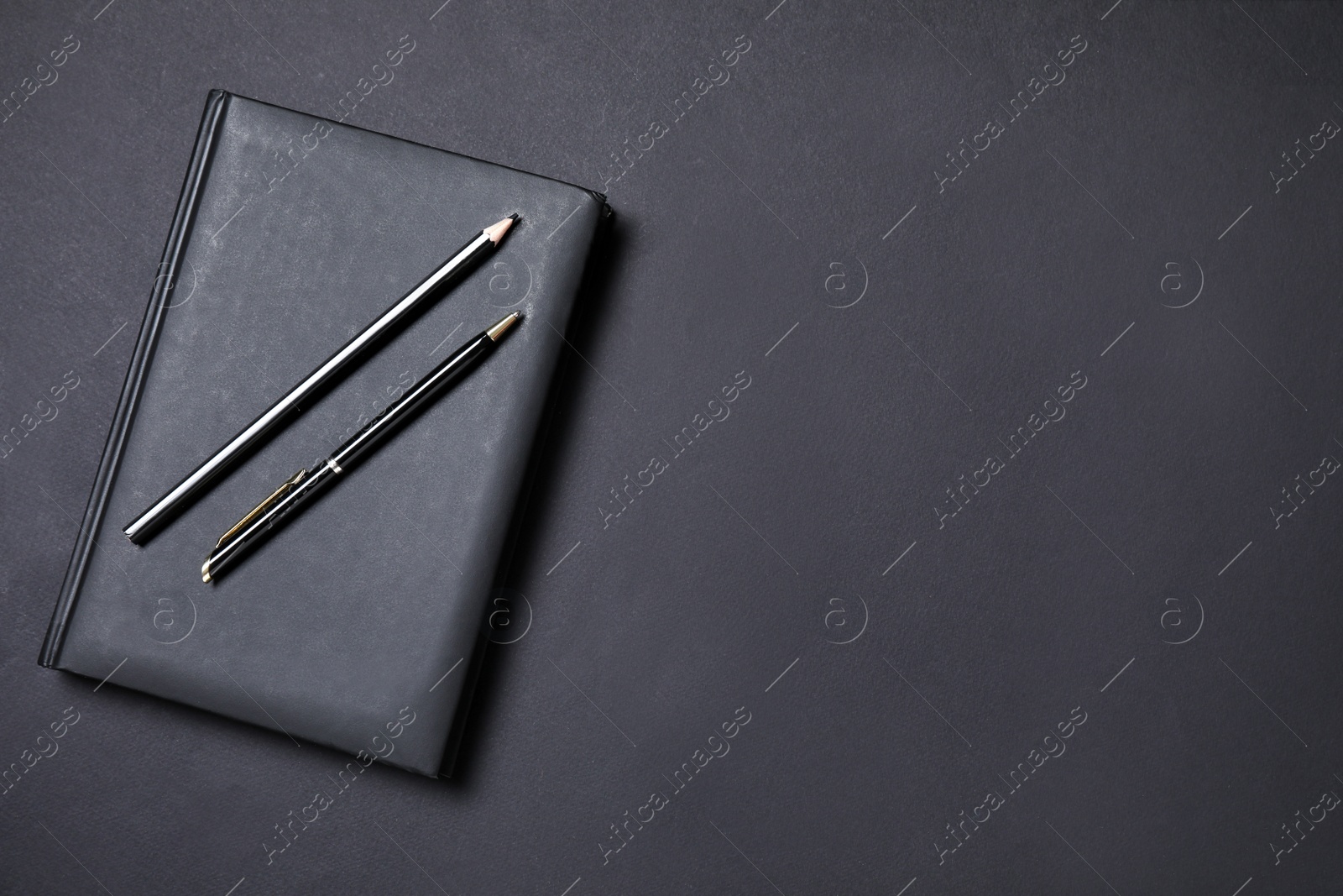 Photo of Notebook, pen and pencil on black background, flat lay. Space for text