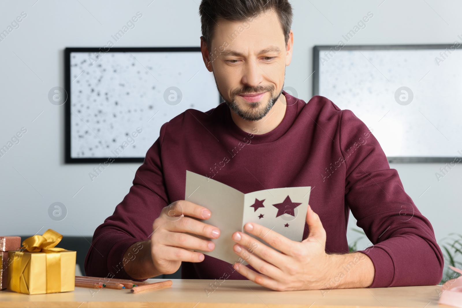 Photo of Happy man reading greeting card at wooden table in room