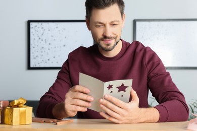 Happy man reading greeting card at wooden table in room