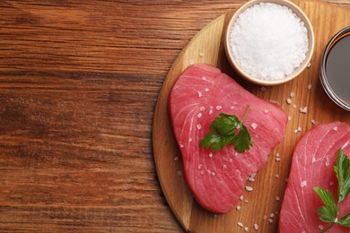 Photo of Raw tuna fillets with parsley, sea salt and soy sauce on wooden table, top view. Space for text