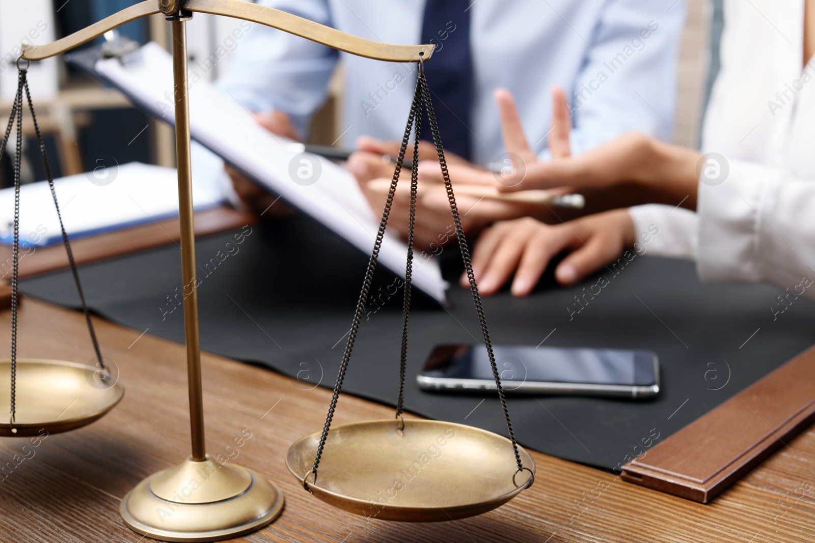 Photo of Scales of justice and blurred lawyer with client on background