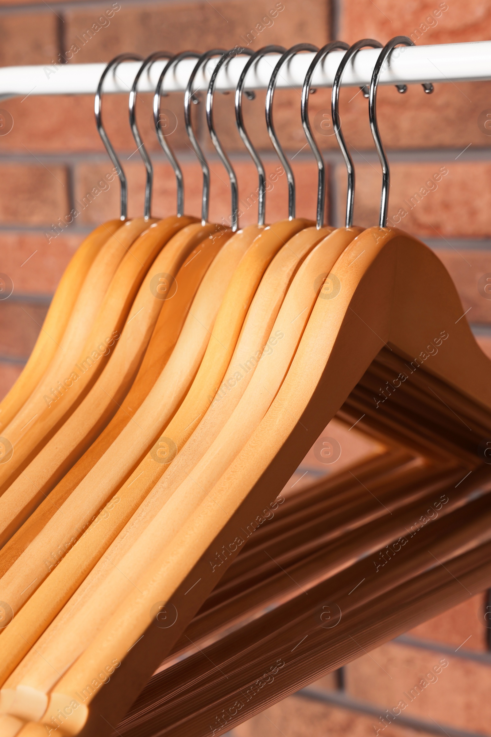 Photo of Wooden clothes hangers on rail near red brick wall, closeup