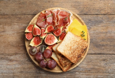 Photo of Delicious ripe figs, prosciutto and cheese served on wooden table, top view