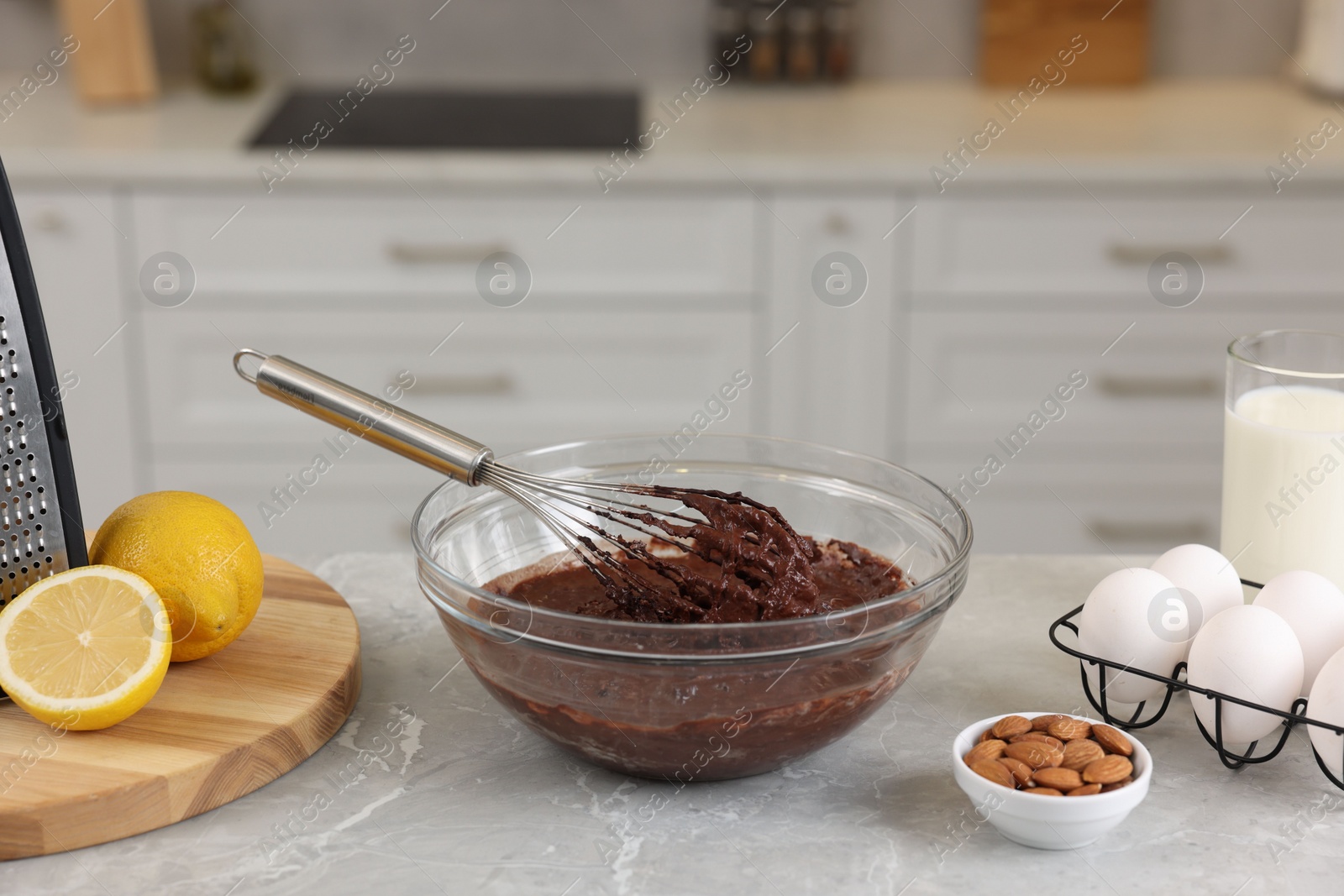 Photo of Metal whisk, chocolate cream in bowl and different products on gray marble table indoors