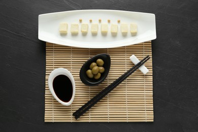 Photo of Cut tofu with soy sauce and olives served on black table, flat lay