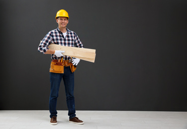 Photo of Handsome carpenter with wooden planks near black wall. Space for text