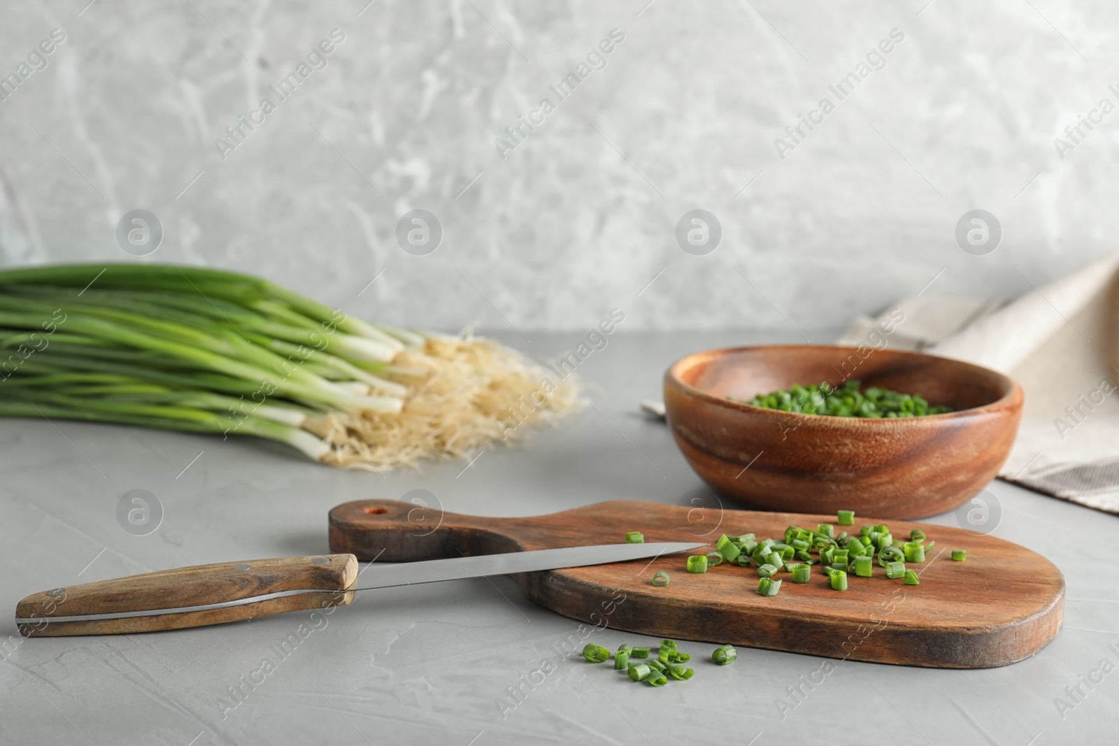 Photo of Wooden board with cut green onion and knife on grey table, space for text