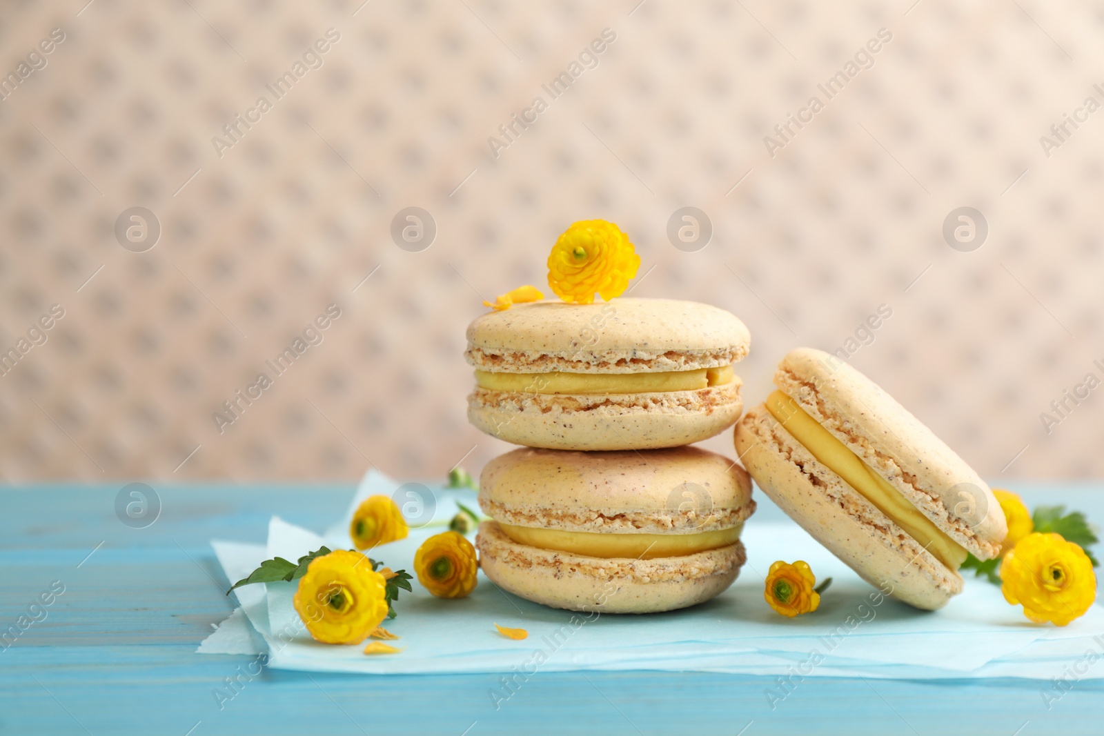 Photo of Delicious macarons and flowers on light blue wooden table