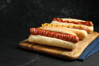 Photo of Fresh delicious hot dogs with sauces on black table