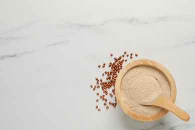 Photo of Buckwheat flour in bowl with wooden spoon on white marble table, flat lay. Space for text