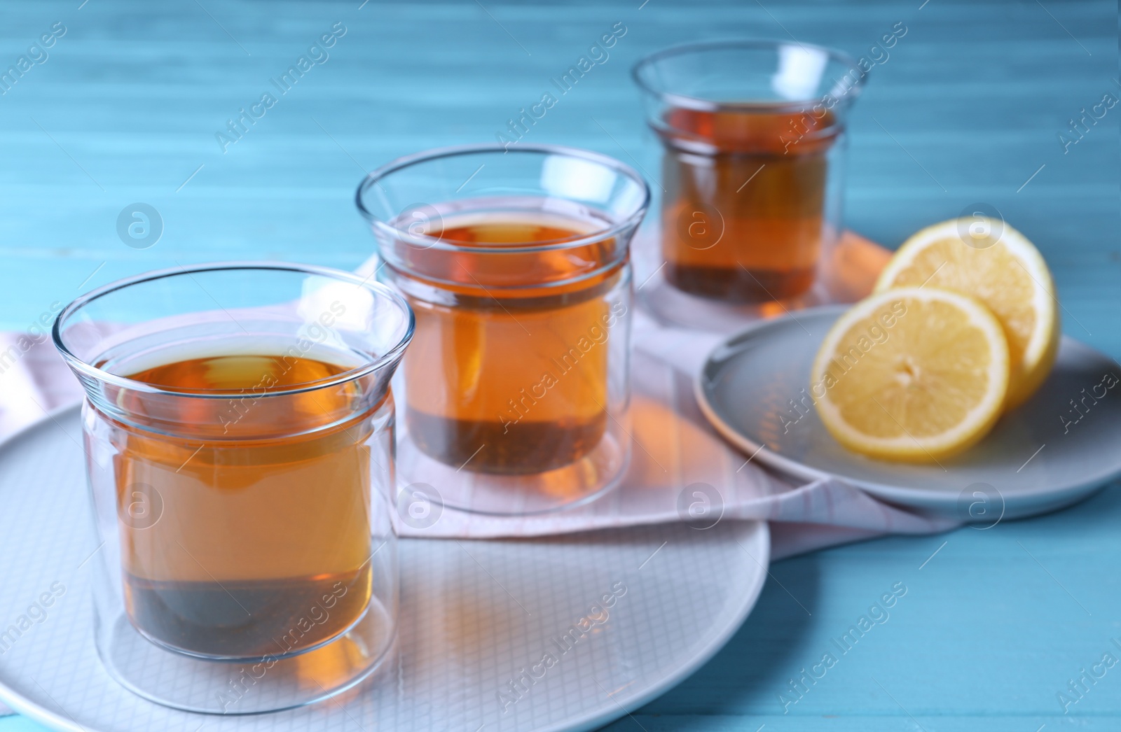 Photo of Plates with glasses of hot tea and lemon on blue wooden table