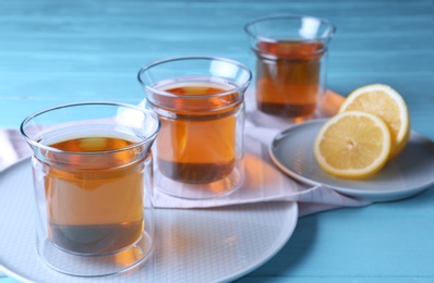 Plates with glasses of hot tea and lemon on blue wooden table