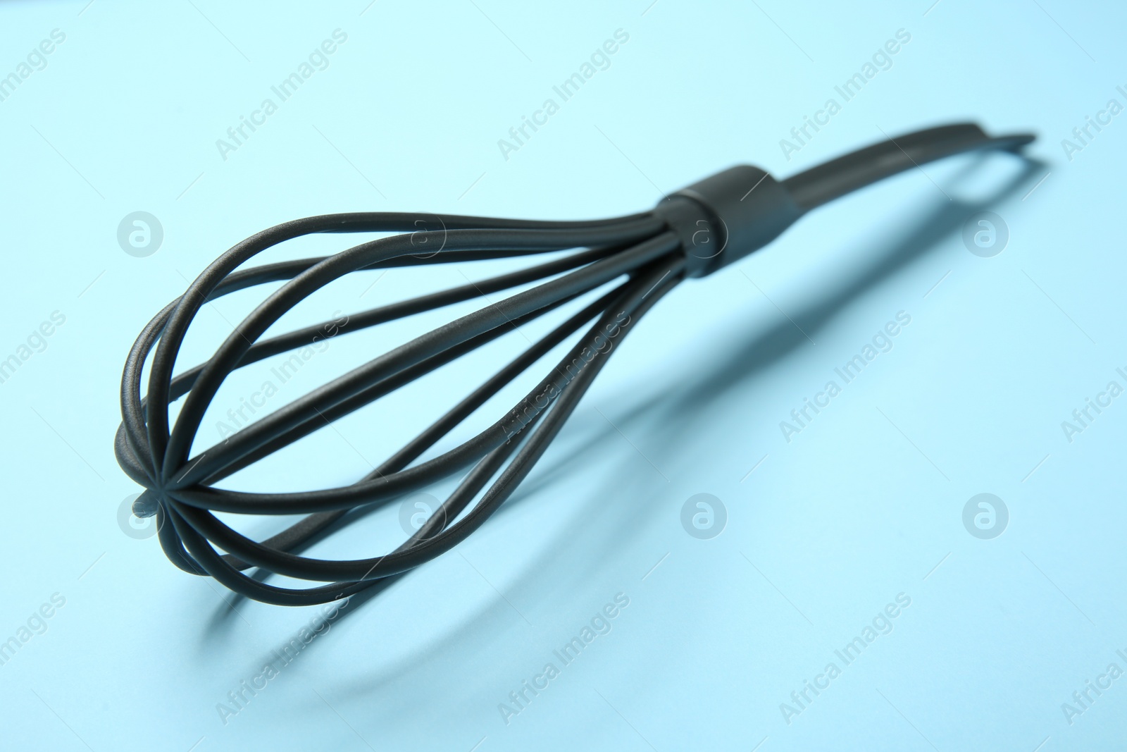 Photo of One whisk on light blue background, closeup