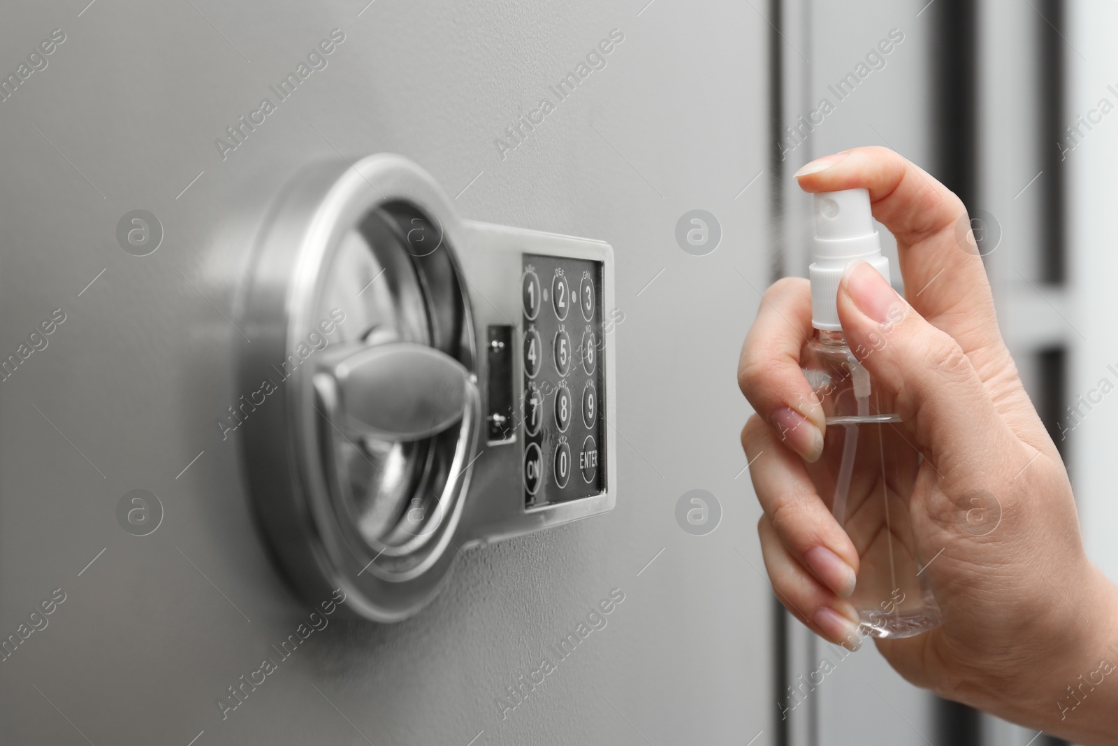 Photo of Woman spraying antiseptic onto keypad of modern safe, closeup