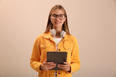 Photo of Teenage student with tablet and headphones on beige background