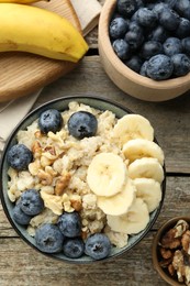 Tasty oatmeal with banana, blueberries and walnuts served in bowl on wooden table, flat lay