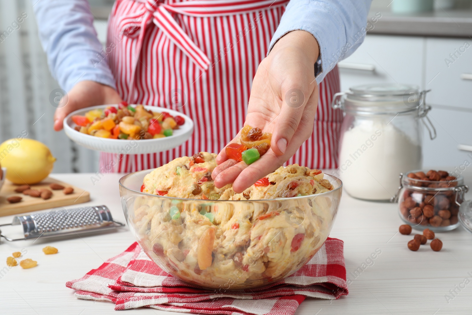 Photo of Woman adding candied fruits to dough for Stollen at white wooden table, closeup. Baking traditional German Christmas bread