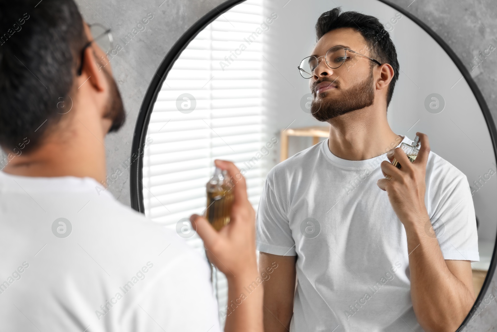 Photo of Man spraying luxury perfume near mirror indoors