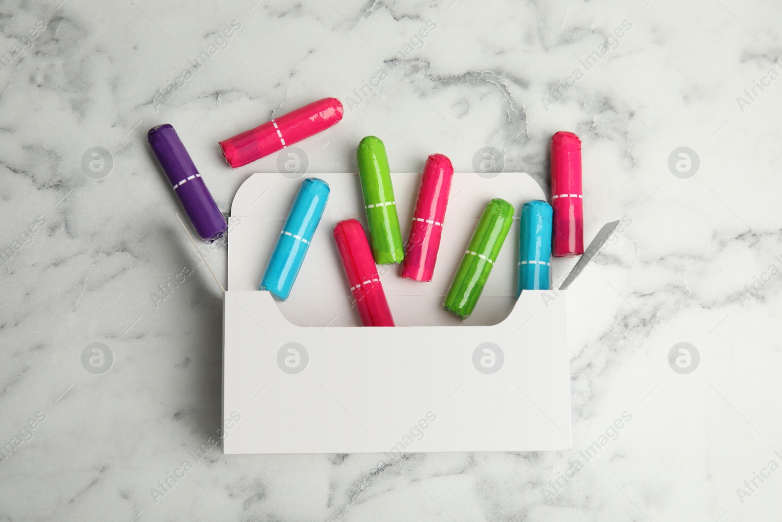 Photo of Pack with colorful tampons on white marble background, flat lay