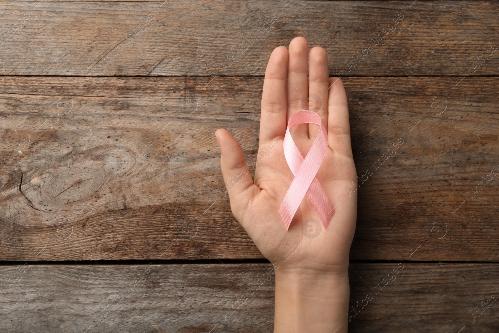 Photo of Woman holding pink ribbon on wooden background, top view with space for text. Breast cancer awareness concept