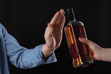 Photo of Alcohol addiction. Man refusing bottle of whiskey on black background, closeup