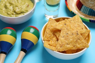 Photo of Nachos chips, Mexican sombrero hat, maracas, guacamole and tequila on light blue background, closeup