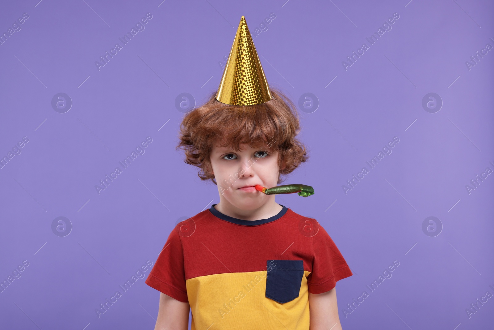 Photo of Sad little boy in party hat with blower on purple background