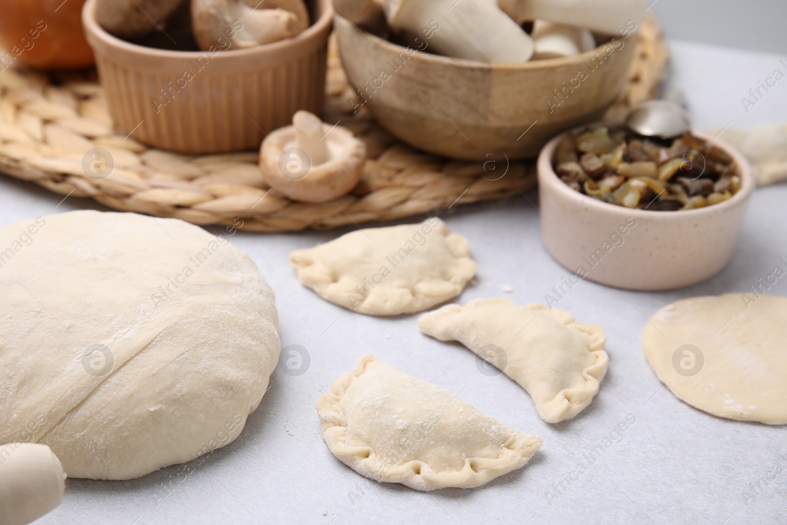 Photo of Process of making dumplings (varenyky) with mushrooms. Raw dough and ingredients on white table, closeup