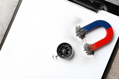 Photo of Compass and magnet with iron powder on clipboard, top view. Space for text