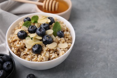 Photo of Tasty oatmeal with blueberries, mint and almond petals in bowl on grey table. Space for text